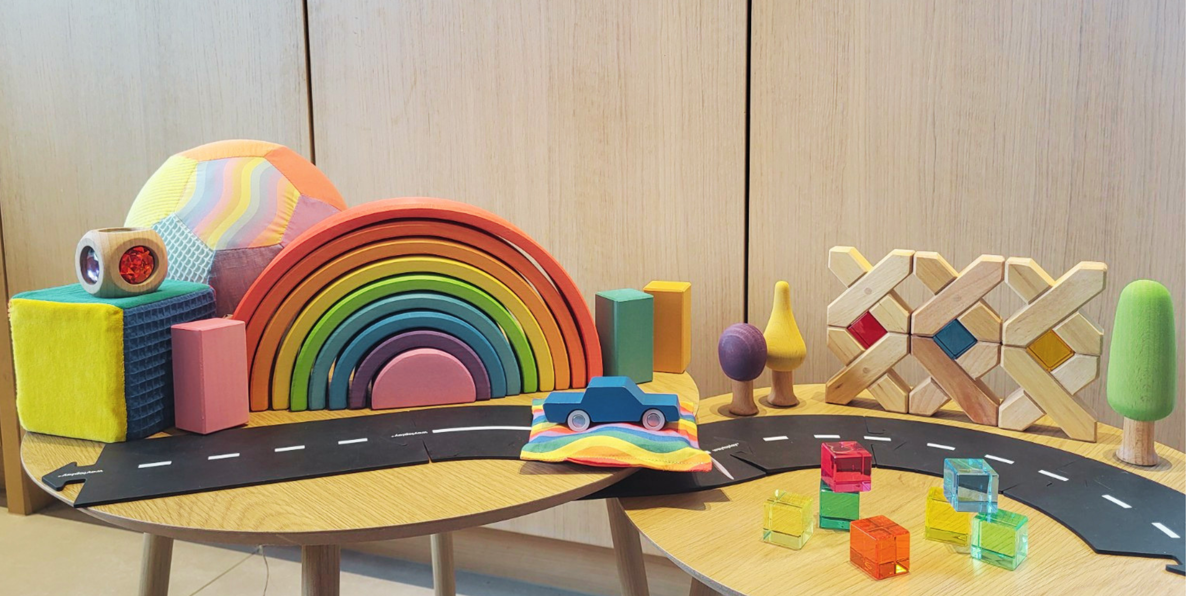 Bannerafbeelding van Intoplay met een selectie open einde speelgoed van verschillende merken, sfeervol gepresenteerd op houten tafeltjes in een rustige en inspirerende speelomgeving.
