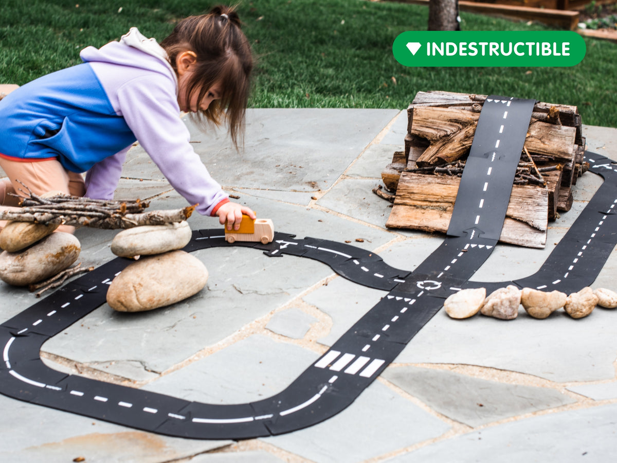 Kind speelt buiten met Waytoplay Highway flexibele autobaan tussen natuurlijke materialen